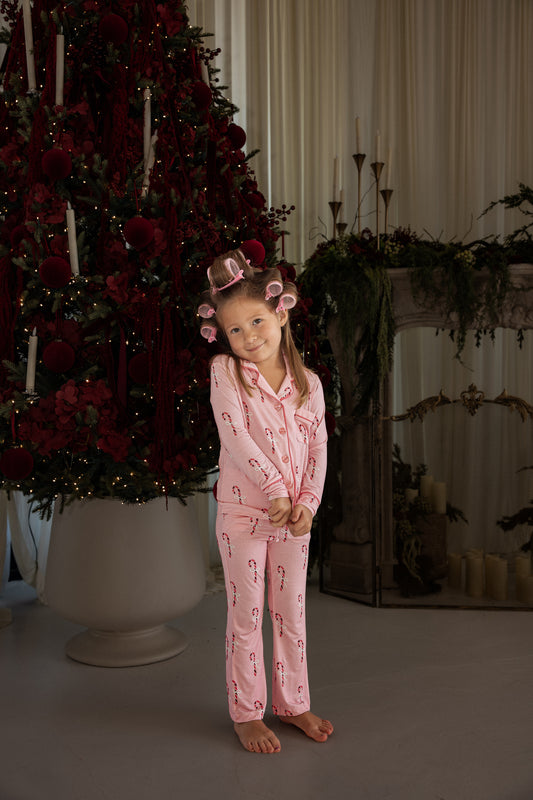 A young girl wearing a Girl’s Bamboo Button Up Lounge Set | Pink Candy Cane with pink hair rollers in her hair.