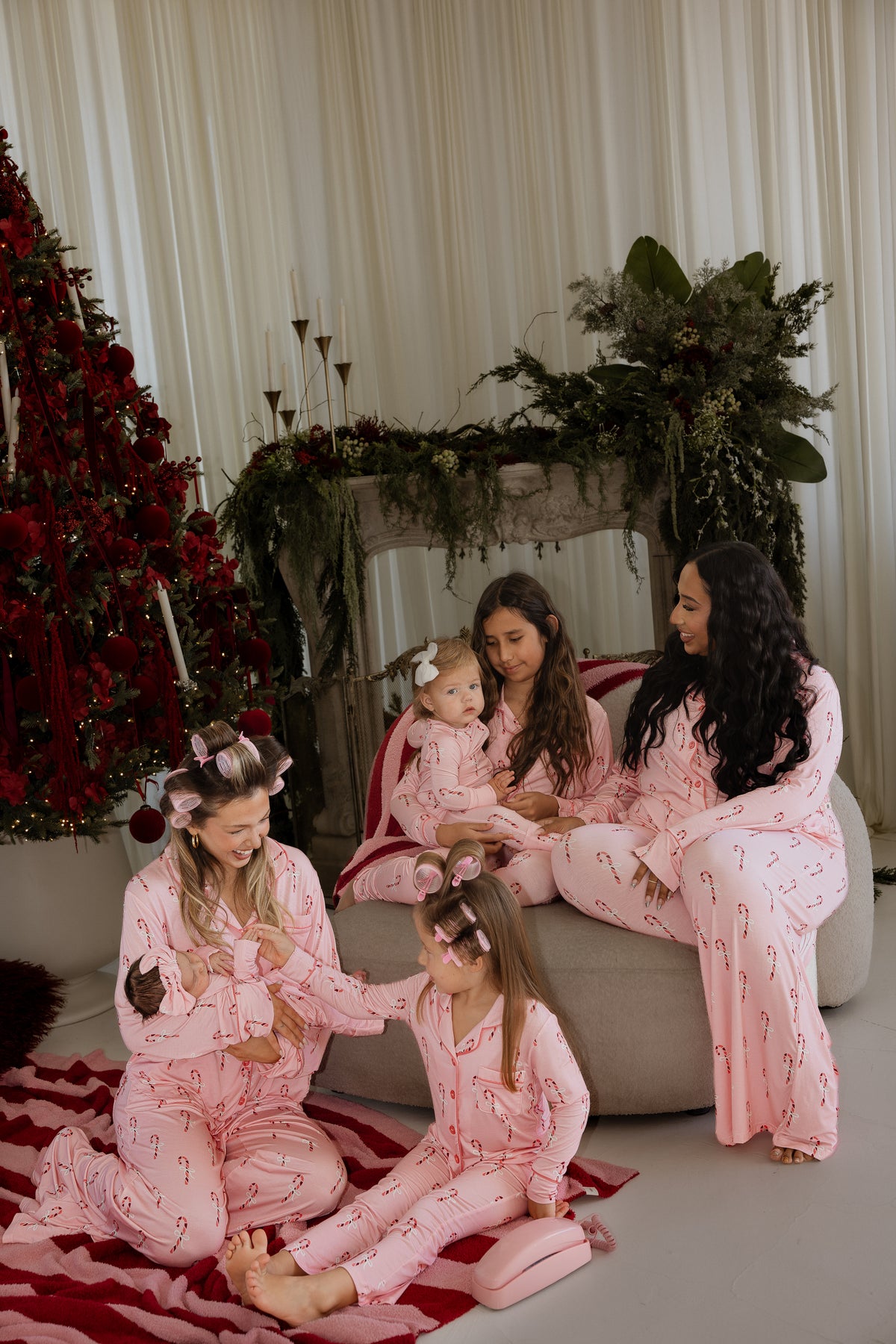 A woman and four children wearing matching Girl’s Bamboo Button Up Lounge Set | Pink Candy Cane outfits, gathered together in a room decorated for Christmas.