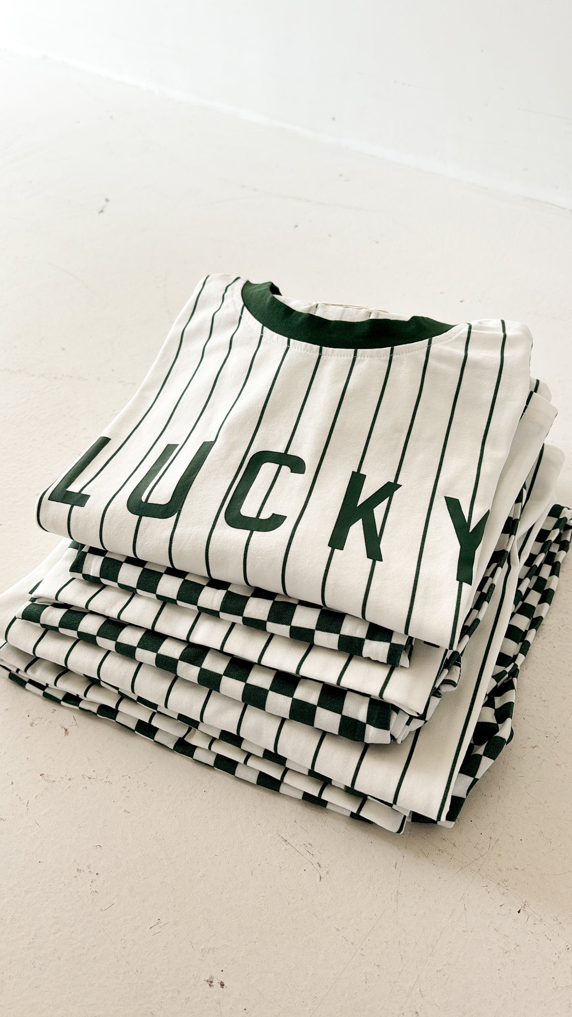 A stack of folded "Lucky" T-shirt & Pant Sets by forever french baby—white shirts with black stripes—ideal for pairing with kids’ wide leg pants or a trendy green micro check look.