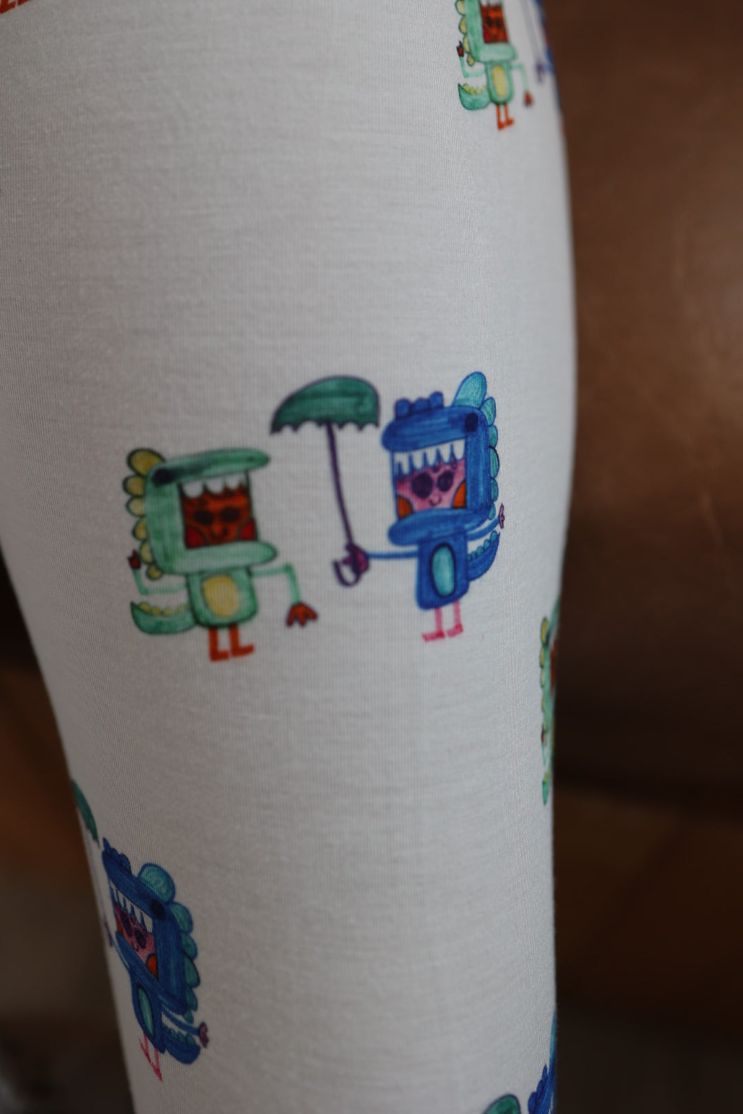 Forever french baby’s Bamboo Two Piece Pajamas | Charli's Monsters feature soft white fabric with colorful cartoon creatures—one green, one blue (holding an umbrella)—in a playful repeating design, perfect for hypoallergenic kids' wear.