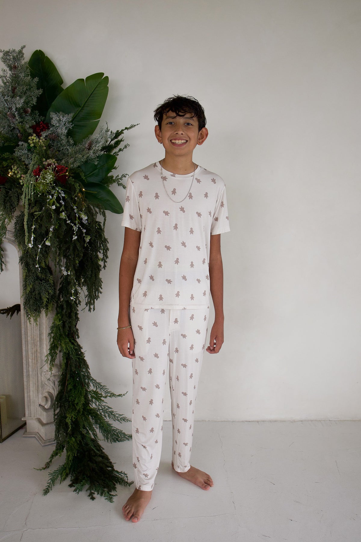 A boy smiles while wearing Youth Straight Leg Bamboo Pajamas in Gingersnap, featuring short-sleeved bamboo pajamas with matching straight-leg pants and an all-over gingerbread man print.