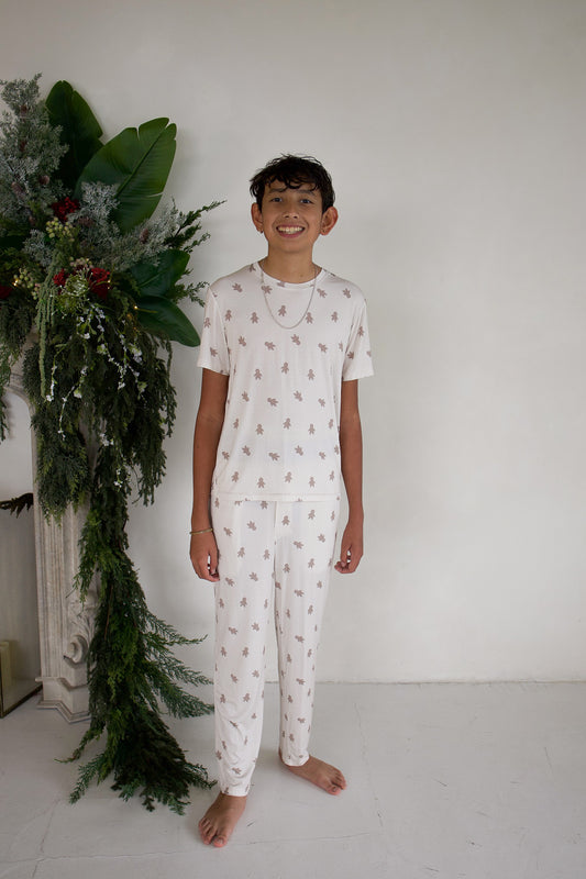 A boy smiles while wearing Youth Straight Leg Bamboo Pajamas in Gingersnap, featuring short-sleeved bamboo pajamas with matching straight-leg pants and an all-over gingerbread man print.
