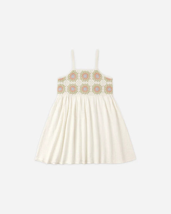 The Rylee + Cru Crochet Sundress | Citron Daisy Check is a white sleeveless mini sundress with thin straps and a gathered skirt. The bodice showcases a colorful, geometric embroidered pattern with circular motifs reminiscent of crochet work. Photographed against a plain light gray background.
