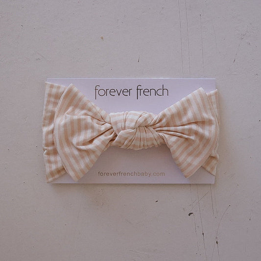 The Bamboo Head Wrap | Sadie Stripe by forever french baby, featuring a peach and white striped design with a large bow, is displayed on branded card packaging against a light background.