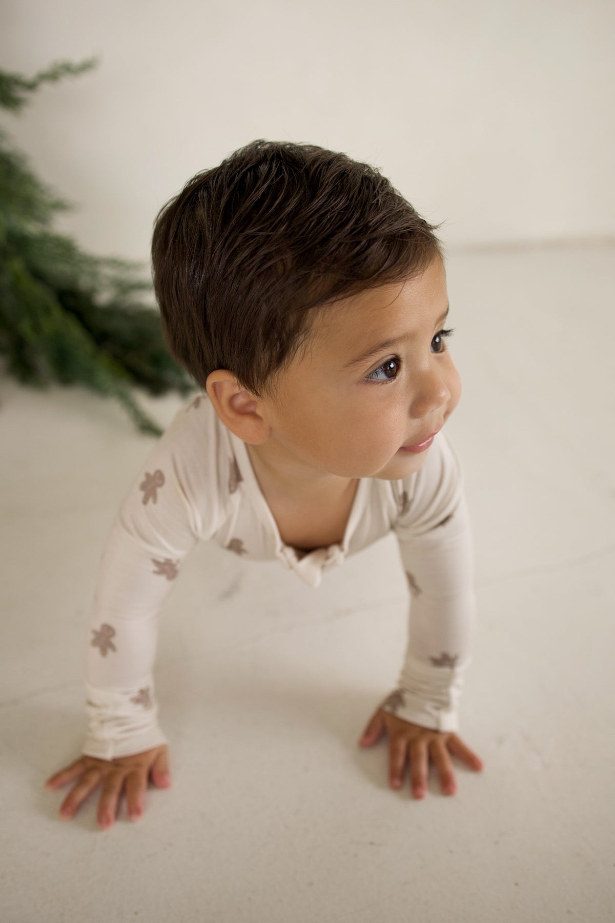 A toddler in Bamboo Zip Pajamas | Gingersnap with a small gingerbread man print crawls on the floor.