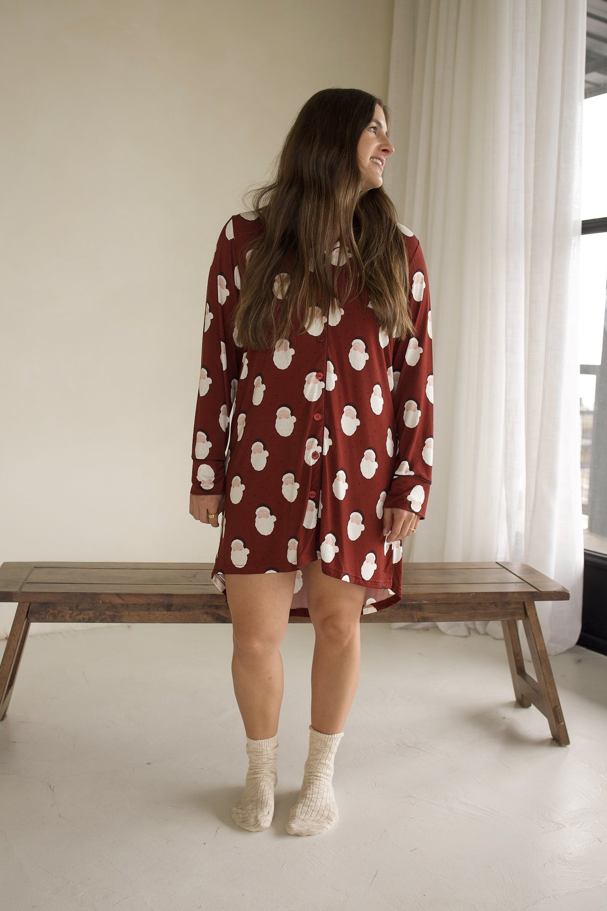 A person wearing a Women’s Bamboo Sleeping Dress | Vintage Santa, a long-sleeved, knee-length maroon button-down dress.