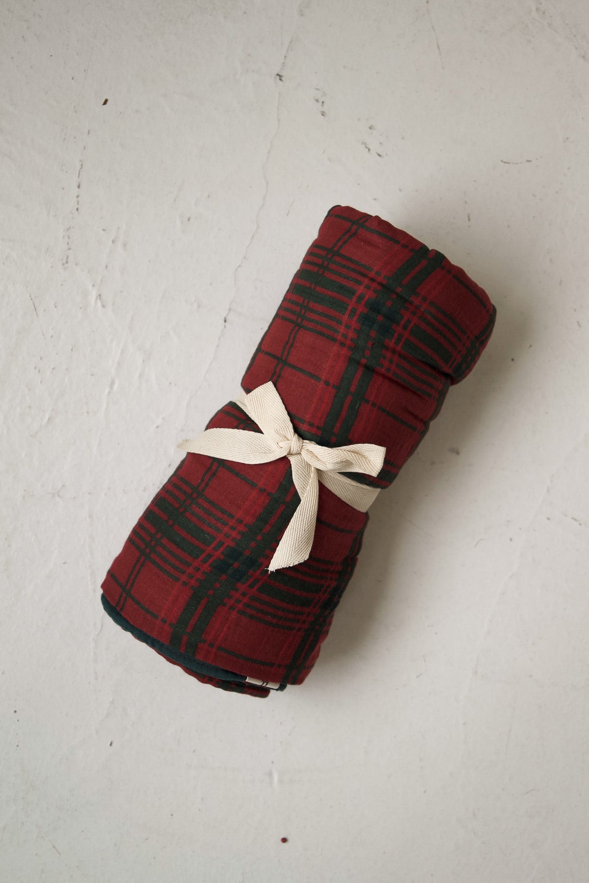 Forever French Baby Muslin Quilt | Christmas Plaid, a rolled red and green Christmas plaid quilt tied with a cream ribbon.