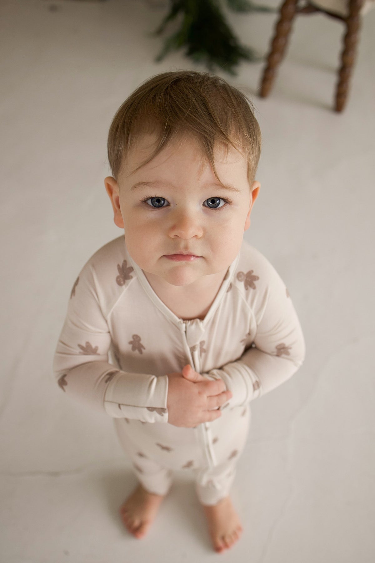 A baby wearing Bamboo Zip Pajamas | Gingersnap with a small gingerbread man print looks up at the camera.