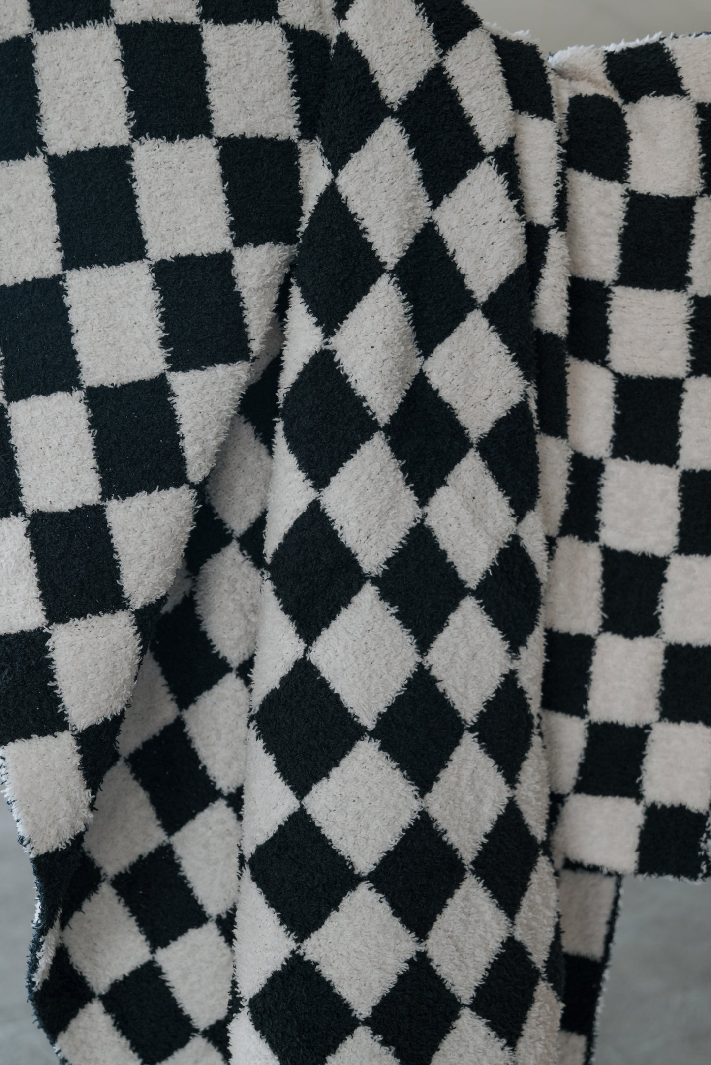 A close-up of the forever french baby Plush Blanket | B&W Micro Check, showcasing its soft, fuzzy microfiber texture and black and white micro check pattern draped in gentle folds.