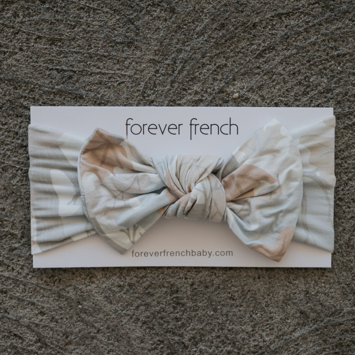 Bamboo Head Wrap | Woodland by forever french baby, featuring a light blue floral design with a large bow, displayed on a branded “forever french baby” card and set on a textured gray surface.