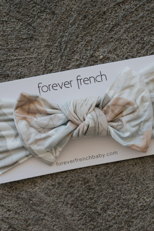 A Bamboo Head Wrap | Woodland from forever french baby, featuring a soft patterned fabric and a large bow, is displayed on a card labeled “forever french” and “foreverfrenchbaby.com” atop a textured gray surface.