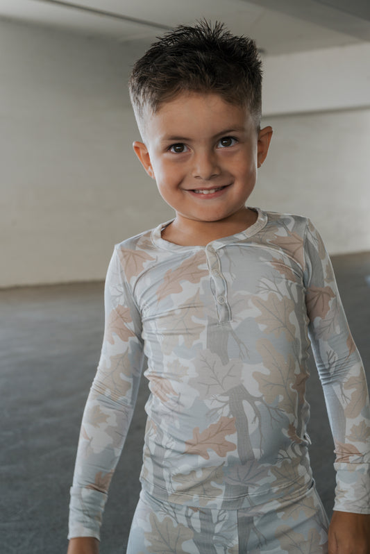 A young child with short brown hair smiles while wearing the Bamboo Two Piece Pajamas in the Woodland print by forever french baby, standing indoors against a plain background—perfectly showcasing the comfort and softness of these hypoallergenic kids pajamas crafted from quality bamboo fabric.