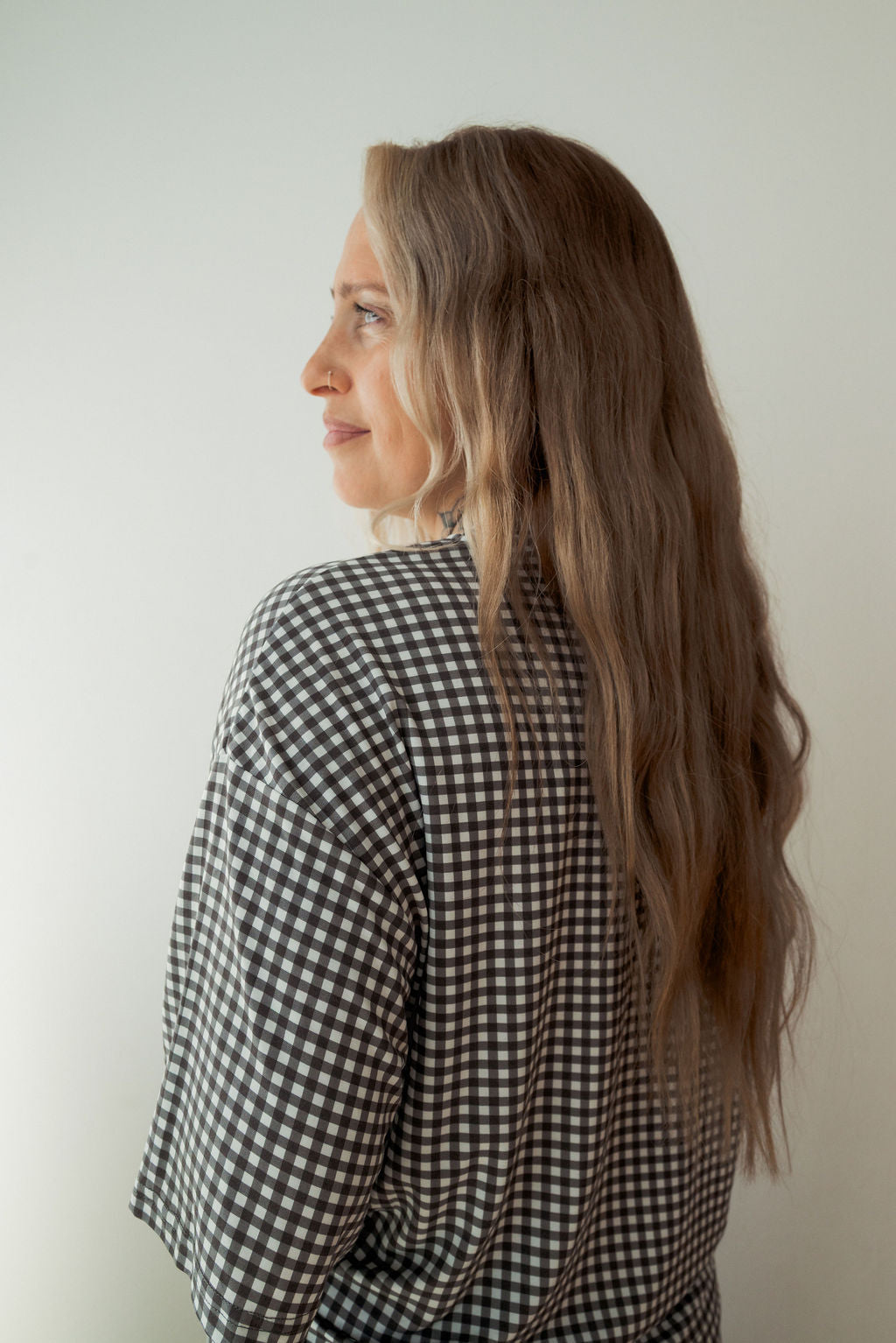 A woman with long, wavy blonde hair stands sideways, smiling slightly. She is wearing the forever french baby Women's Boxy Tee Lounge Set in Green Gingham against a plain, light-colored background.