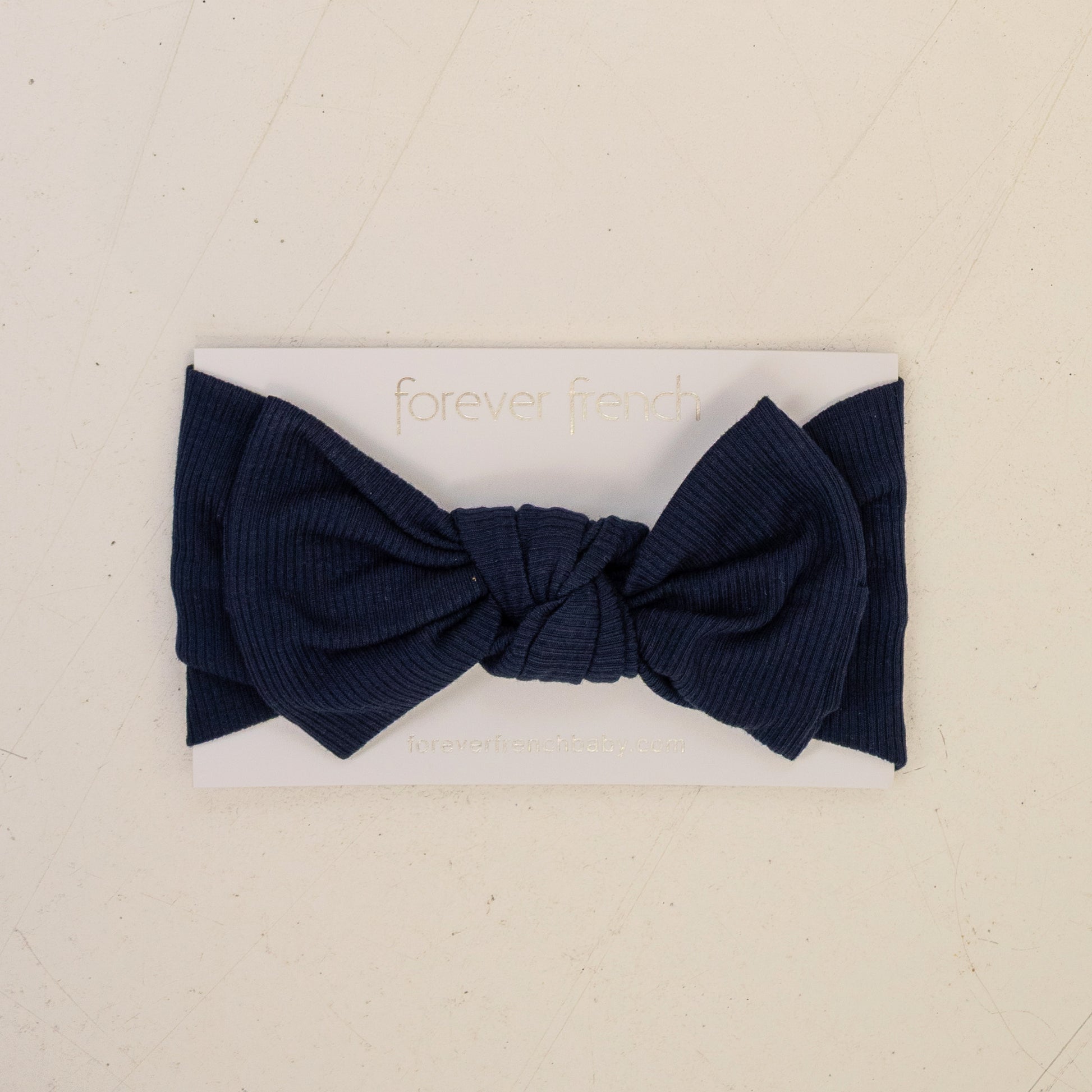 The Bamboo Head Wrap | Blueberry Ribbed by forever french baby features a large navy ribbed bow, shown on a white branded card against a light beige background.
