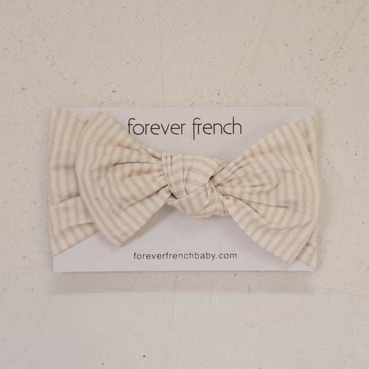 The Bamboo Head Wrap | Teddy by forever french baby, featuring beige and white stripes and a large bow, is displayed on branded packaging with "foreverfrenchbaby.com" against a light textured background.