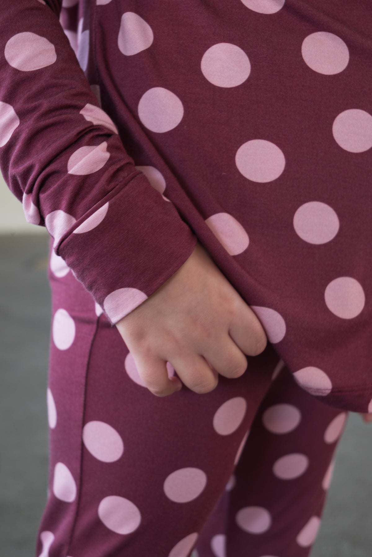 A person wearing the forever french baby Girl’s Bamboo Button Up Lounge Set in Heather Rose Dot stands with one hand holding the hem of their top, enjoying the soft, hypo-allergenic comfort of bamboo clothing.