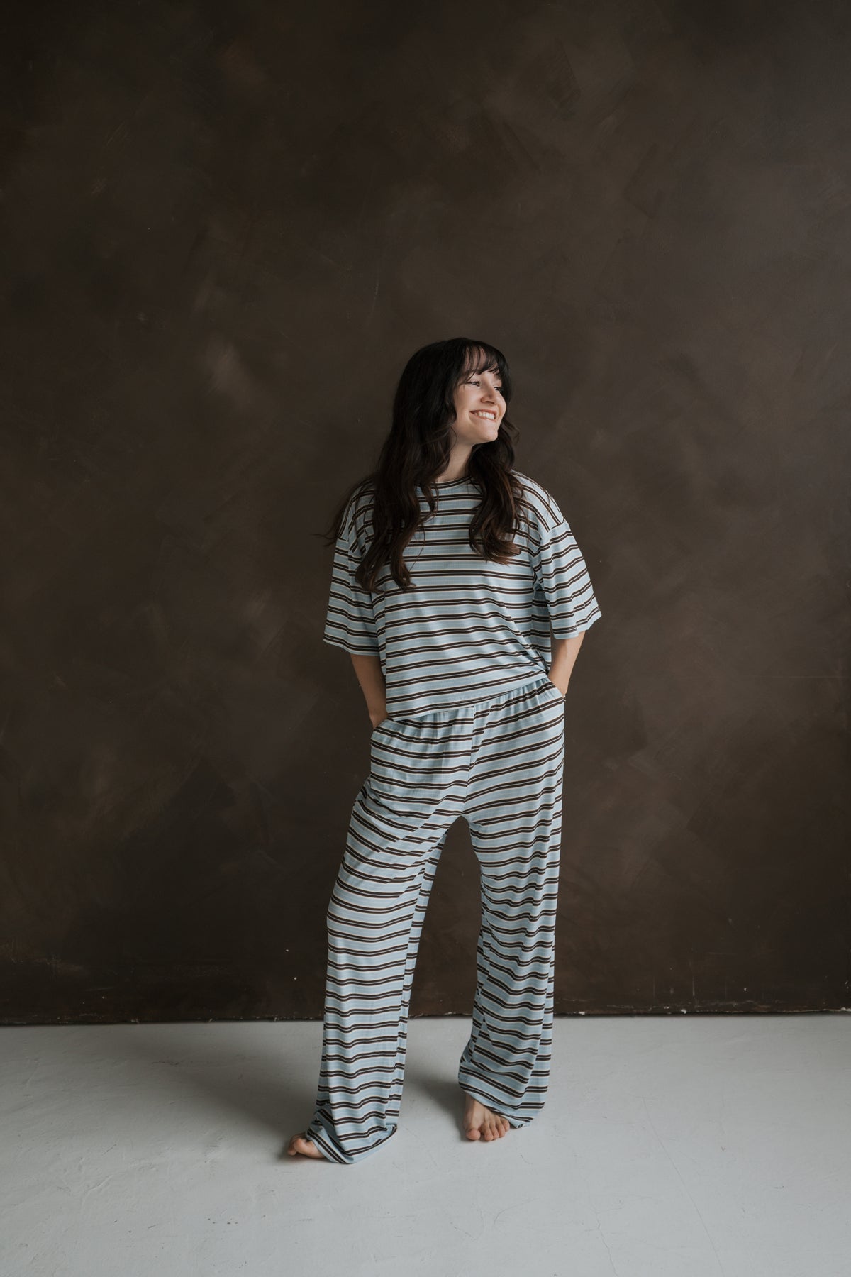 A woman smiling while wearing a Women’s Boxy Tee Lounge Set | Dean in a breathable, light blue and brown striped short-sleeved top and matching wide-leg lounge pants.