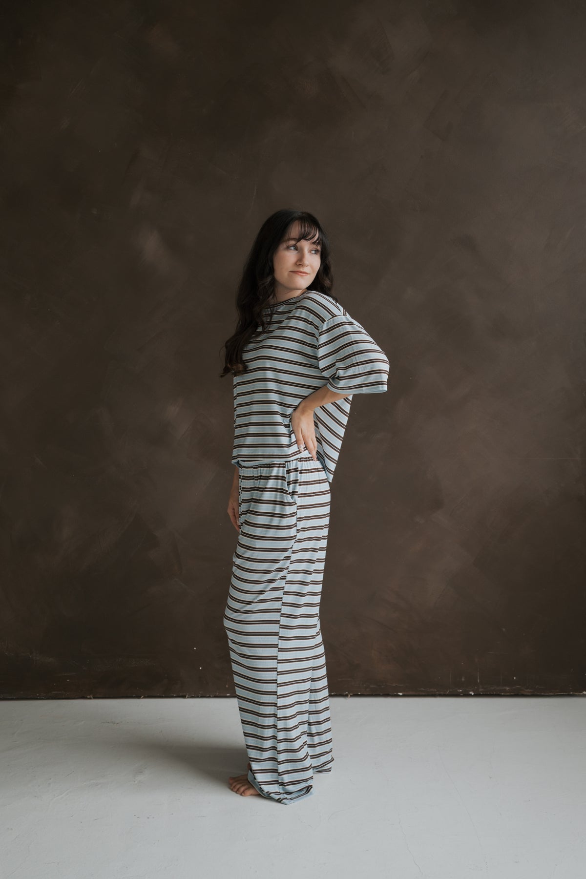 A woman wears a light blue and brown horizontally striped Women’s Boxy Tee Lounge Set | Dean, featuring a breathable short-sleeved top and loose-fitting pants.
