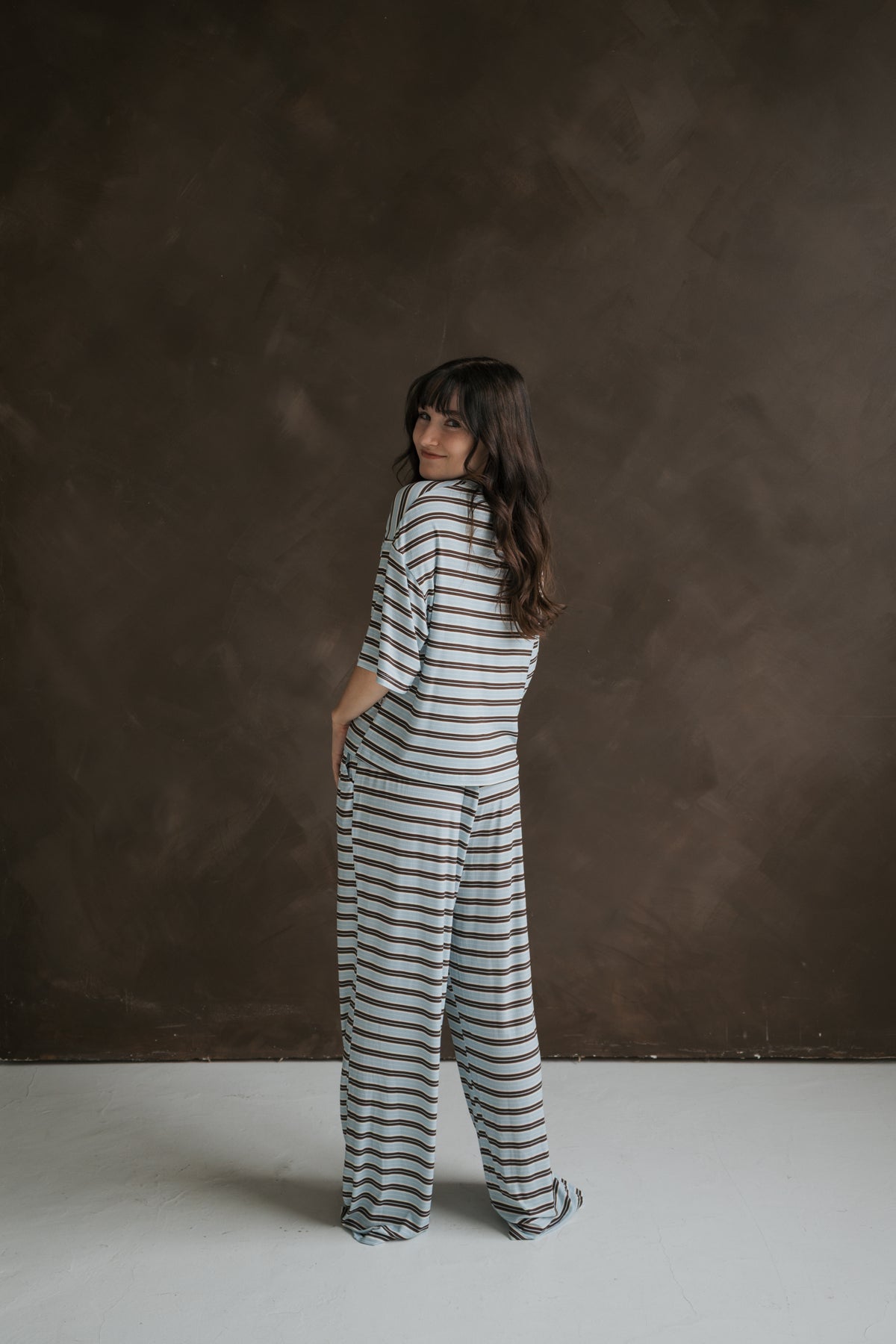 A woman wears the forever french baby Women’s Boxy Tee Lounge Set in light blue with thin brown horizontal stripes, consisting of a boxy short-sleeved top and wide-leg pants.
