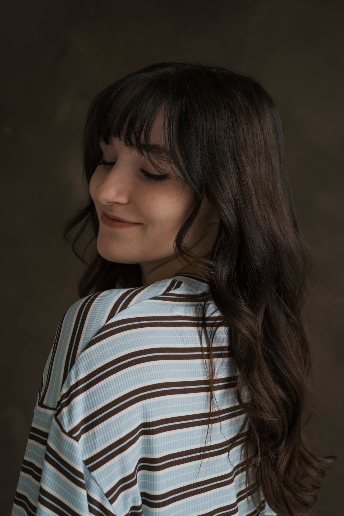 A woman with long, dark hair looks over her shoulder while wearing the blue and brown striped Women’s Boxy Tee Lounge Set | Dean.