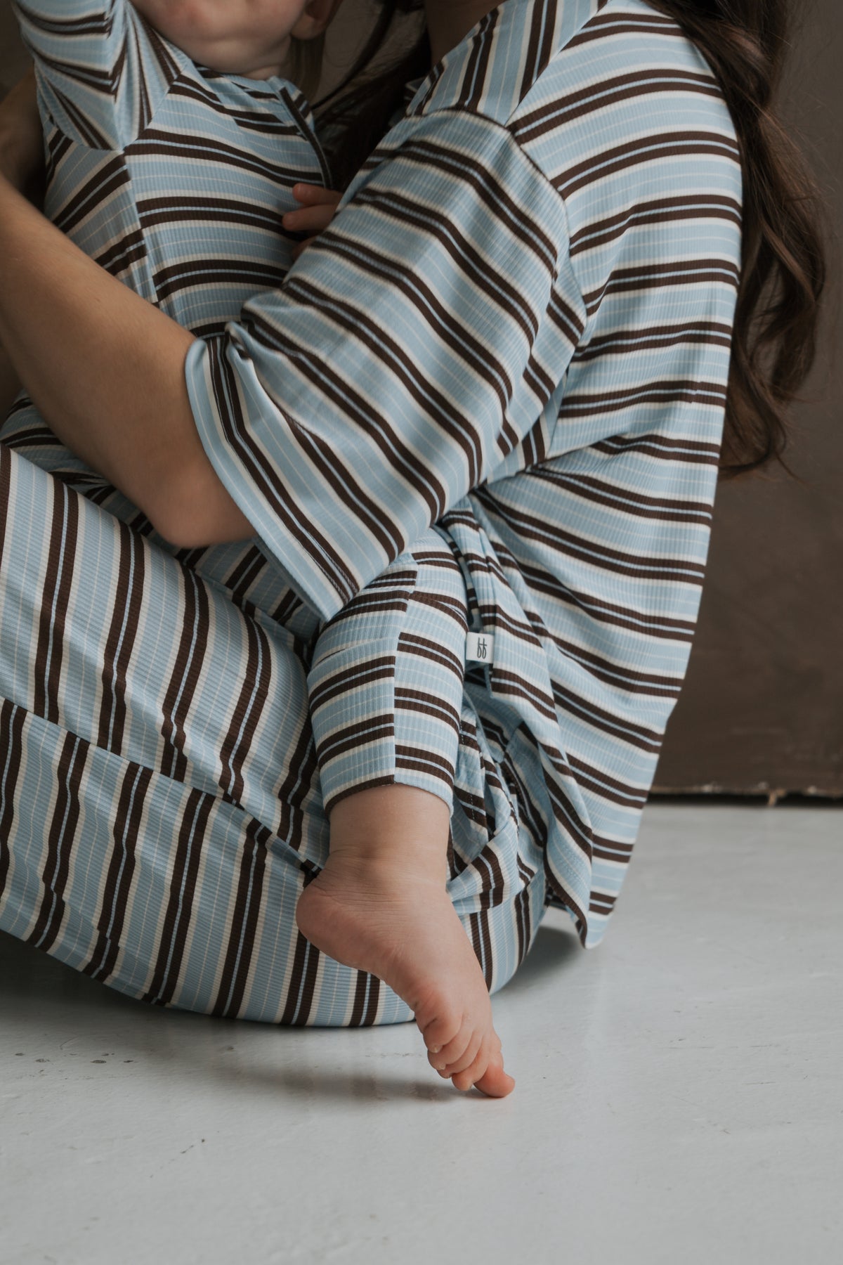 A person holds a toddler, both wearing matching Bamboo Zip Pajamas | Dean in a blue and brown ribbed striped pattern.