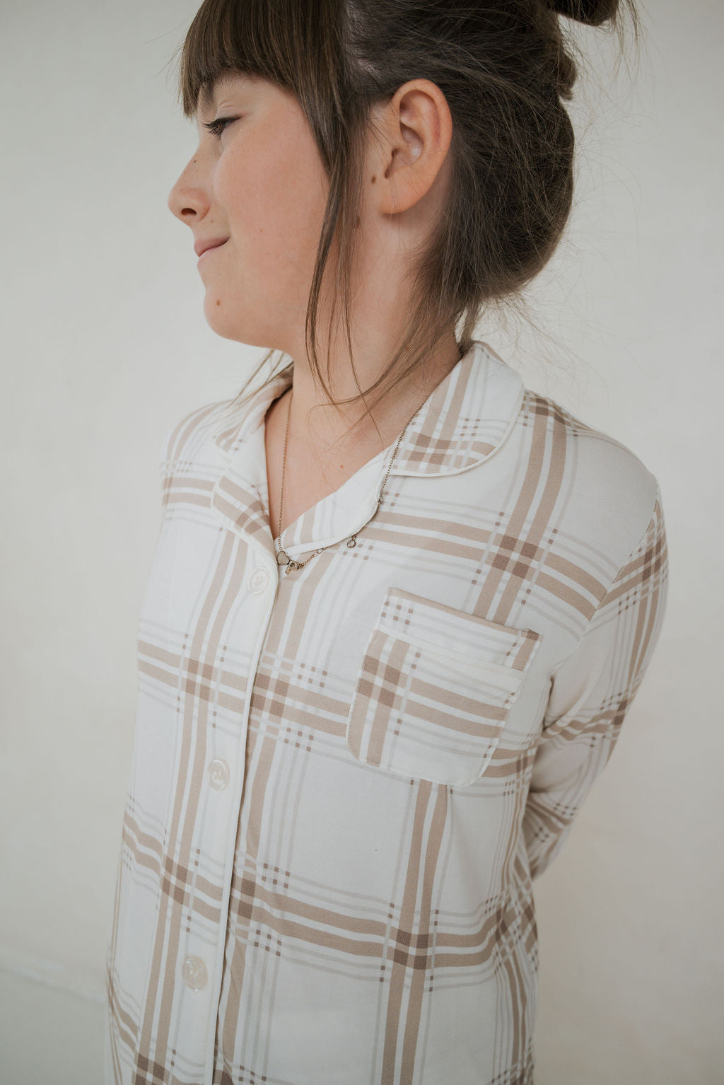 A child wears the Girl’s Bamboo Button Up Lounge Set | Ellis Plaid by forever french baby—a cozy cream and tan plaid pajama top with chest pocket, perfect for sleep or matching family outfits in soft bamboo.