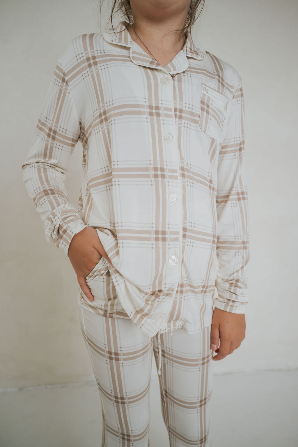 Child wearing the Girl’s Bamboo Button Up Lounge Set in Ellis Plaid, featuring a long-sleeved button-up shirt and pants in a tan and cream plaid pattern.
