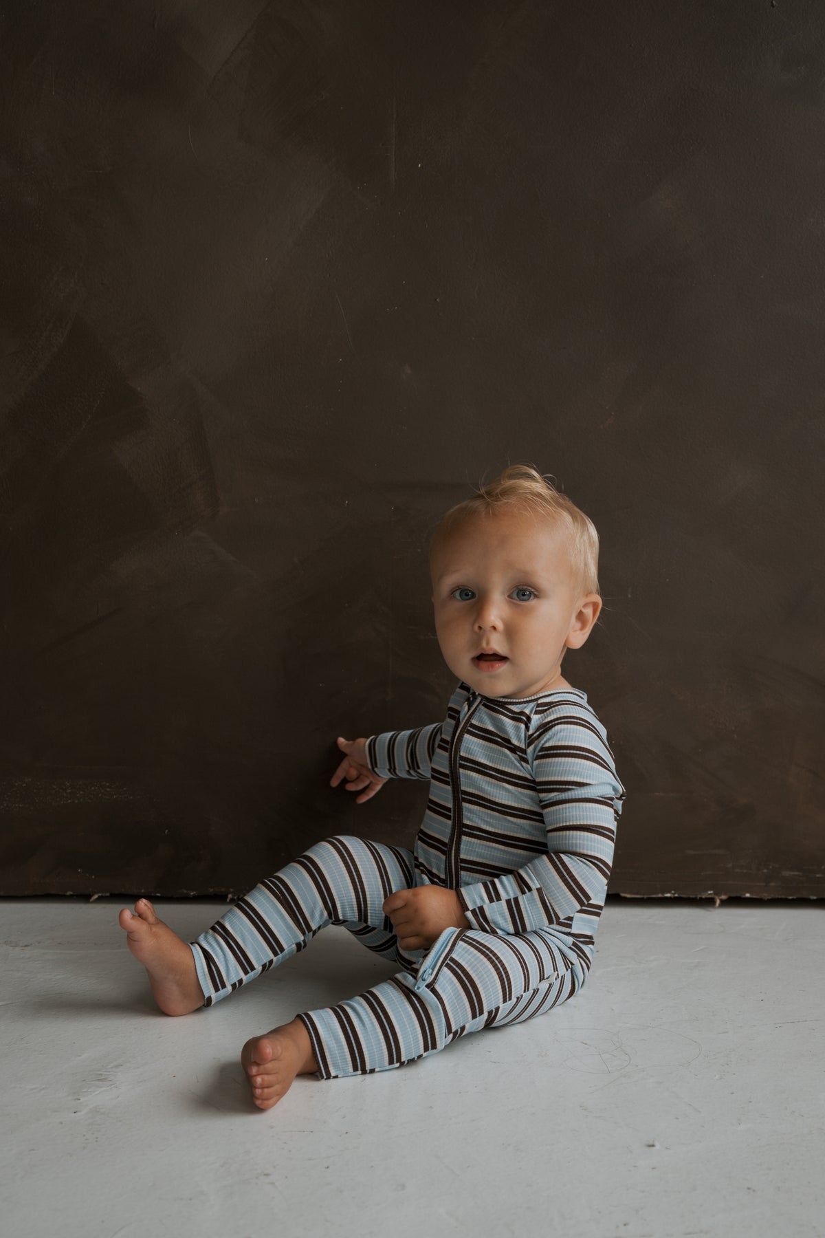 A toddler sitting on the floor wearing blue and brown striped ribbed Bamboo Zip Pajamas | Dean.