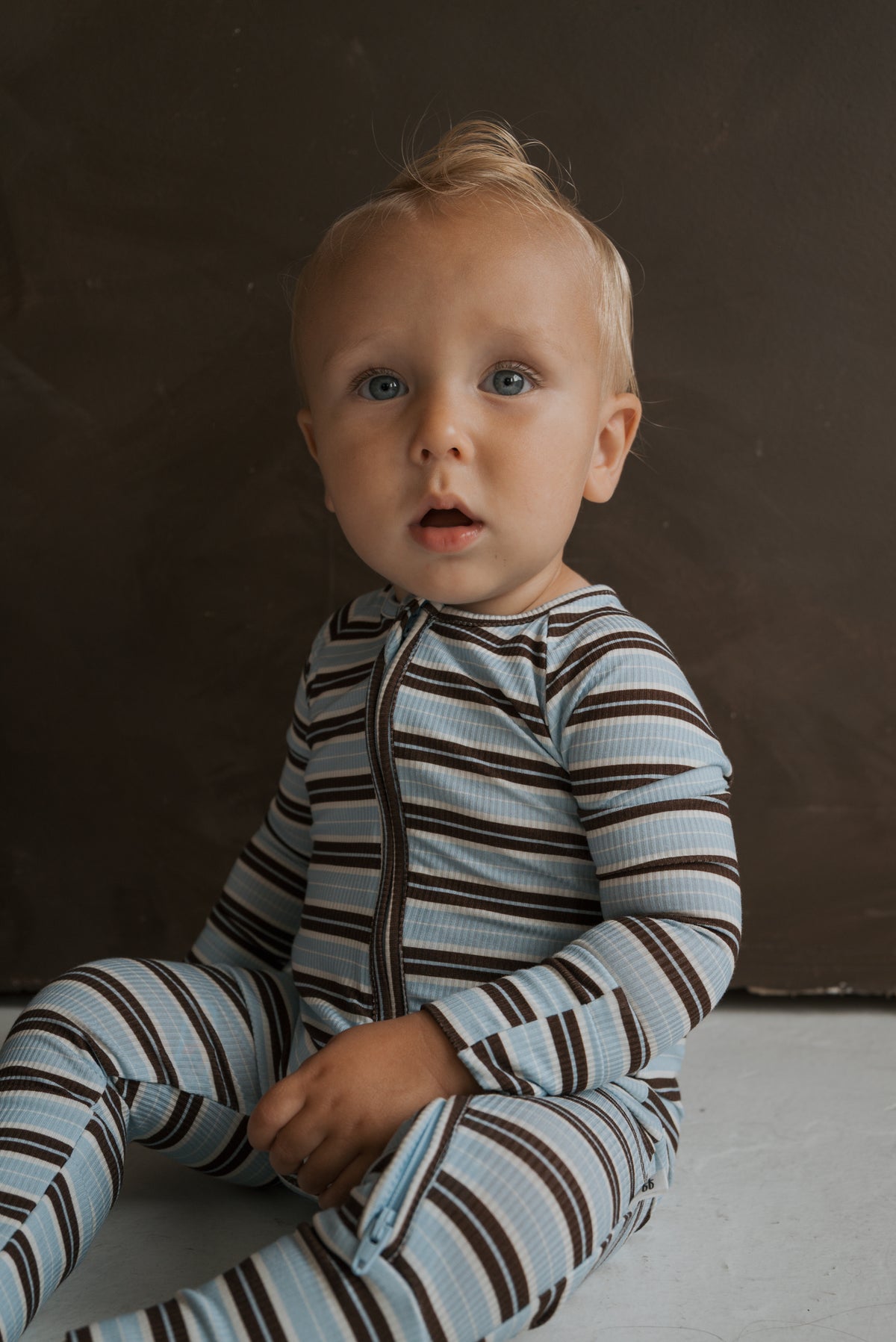 A young child wearing blue and brown striped ribbed Bamboo Zip Pajamas | Dean with a zip-front.
