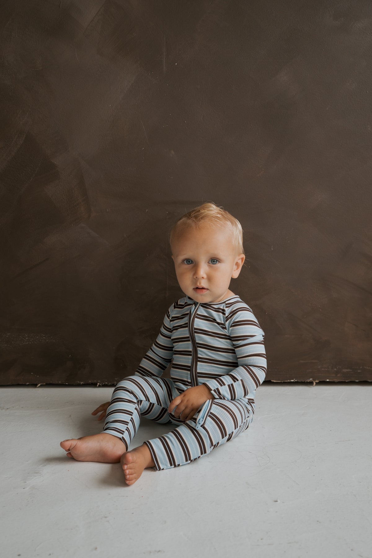 A toddler sits on the floor wearing blue and brown striped ribbed Bamboo Zip Pajamas | Dean by forever french baby.