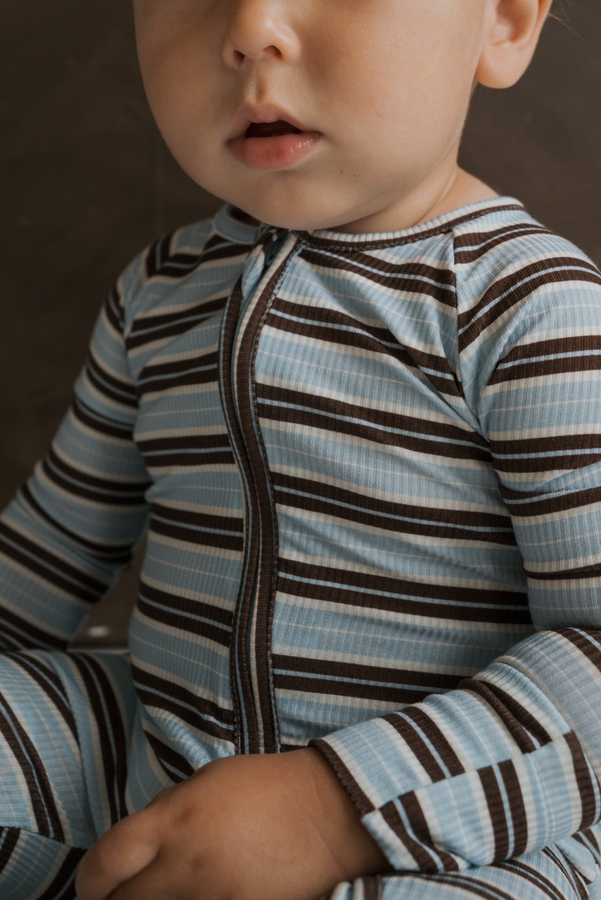 A toddler wears Bamboo Zip Pajamas | Dean featuring horizontal blue, brown, and white ribbed bamboo stripes with a center front zipper.