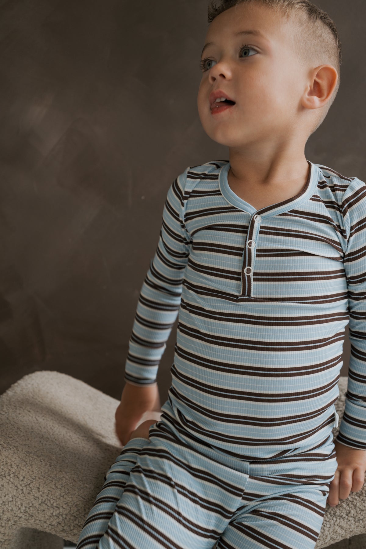 A young boy wearing a Bamboo Two Piece Pajamas | Dean set in blue and brown stripes with a button placket.
