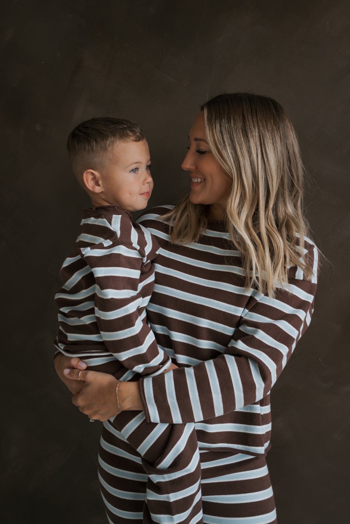 A woman holds a young boy, both wearing matching brown and light blue Knit Pant Set | Garrett *PRE-ORDER* knit sets for their fall wardrobe.
