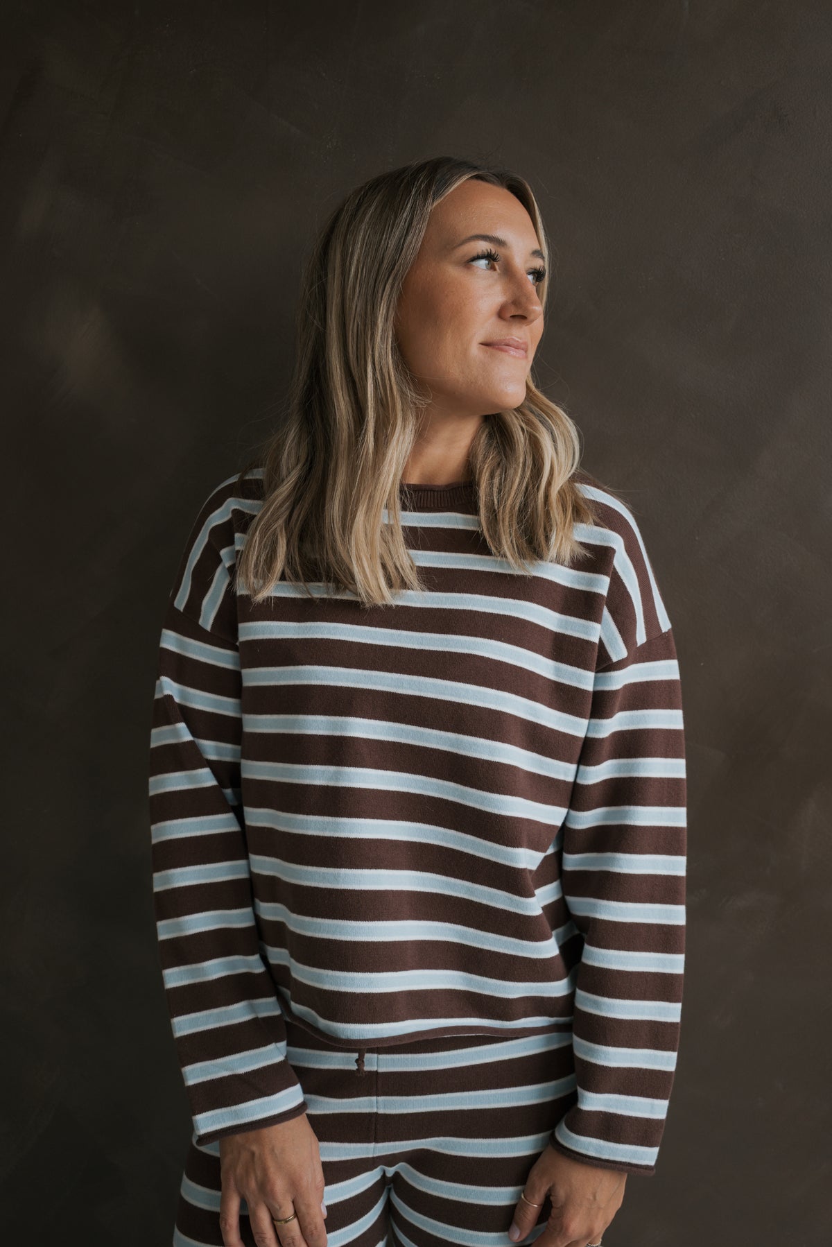 A woman wearing the Women’s Knit Pant Set | Garrett *PRE-ORDER*, featuring an oversized, long-sleeved knit top and matching pants in a brown and light blue striped pattern.