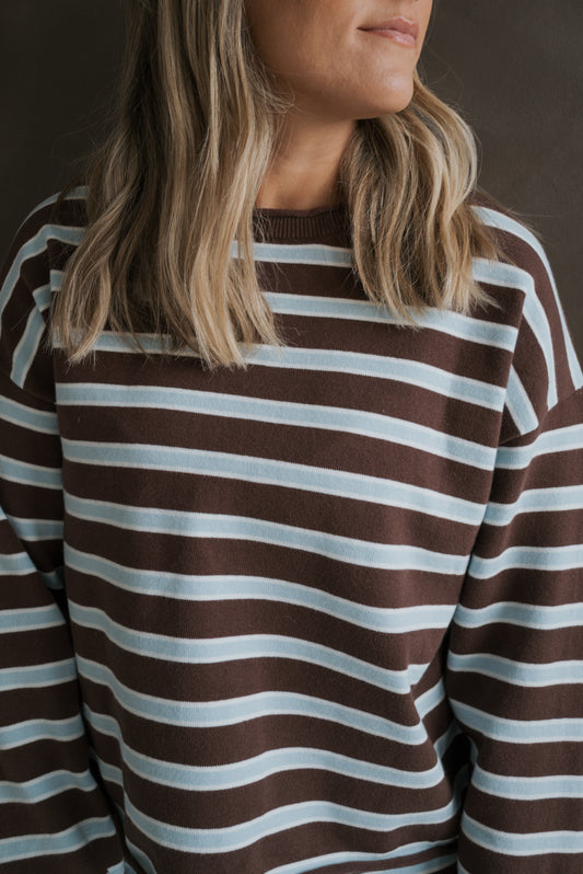 A person wearing the Women’s Knit Pant Set | Garrett *PRE-ORDER* featuring an oversized, long-sleeved sweater with horizontal brown and light blue stripes.