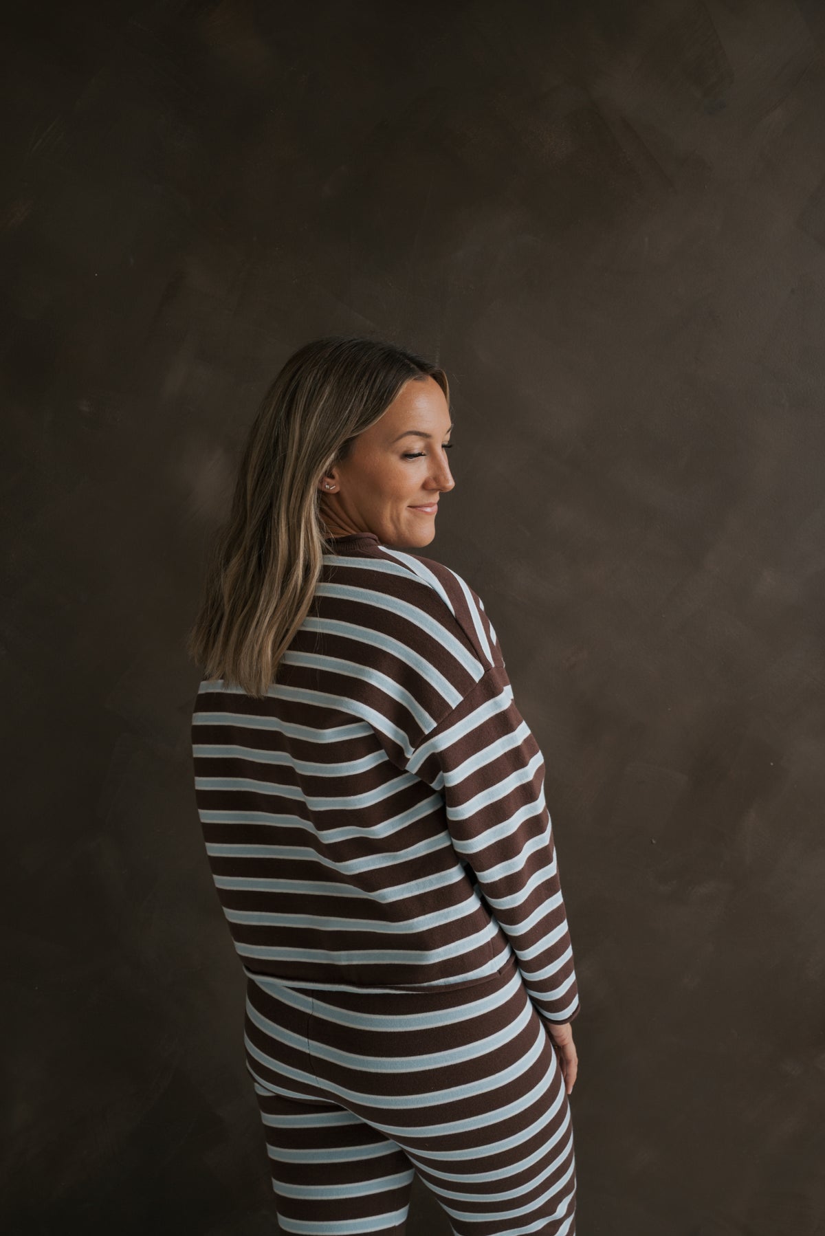 A woman seen from behind wearing the Women’s Knit Pant Set | Garrett by forever french baby, an oversized brown and light blue striped knit set consisting of a long-sleeved shirt and matching pants.