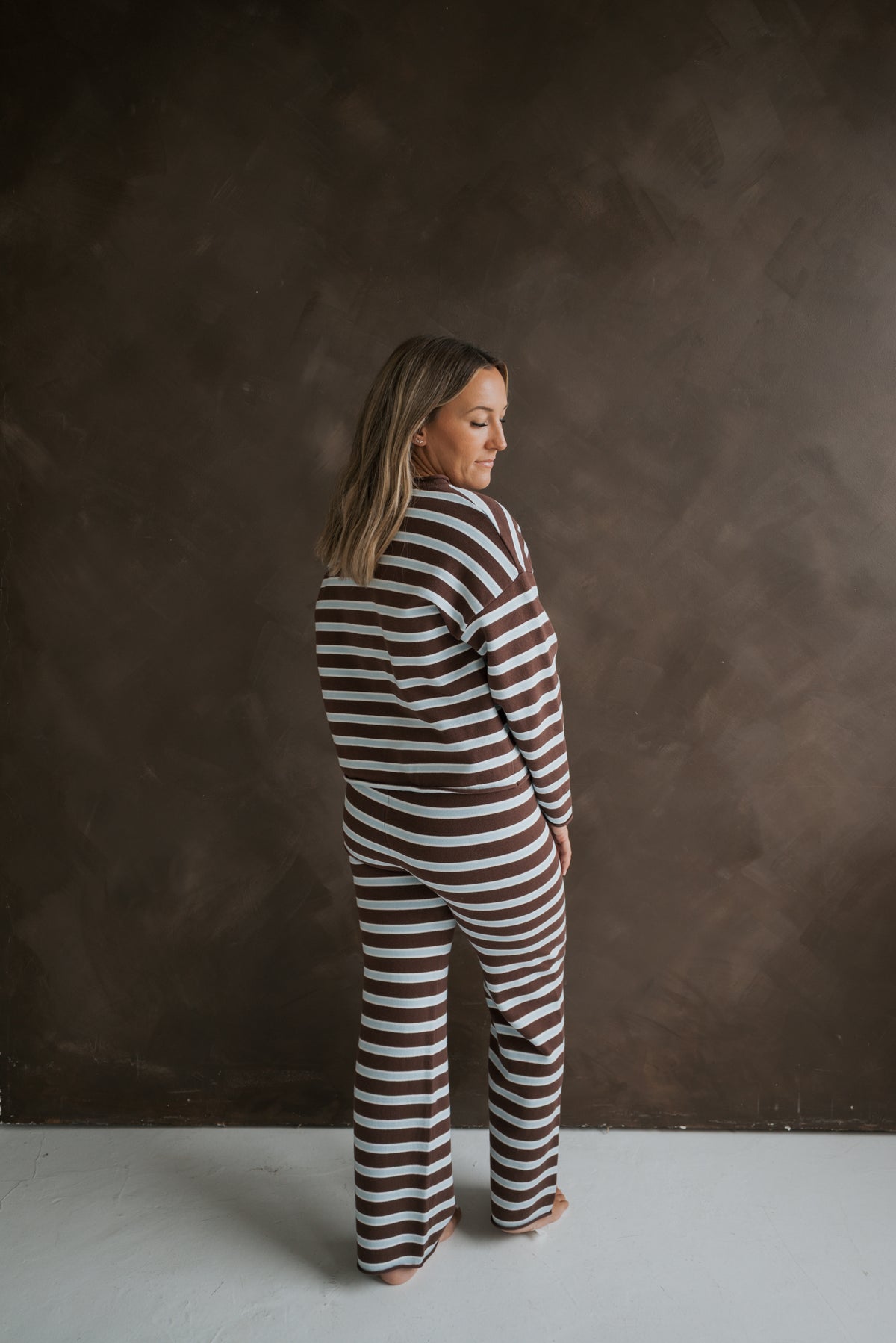 A person wears the Women’s Knit Pant Set | Garrett *PRE-ORDER* in an oversized top and pants featuring a matching brown and white horizontal stripe knit pattern.