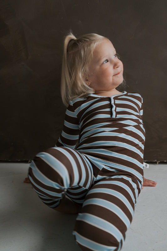 A young child sits on the floor wearing brown and light blue striped Bamboo Two Piece Pajamas | Garrett by forever french baby.