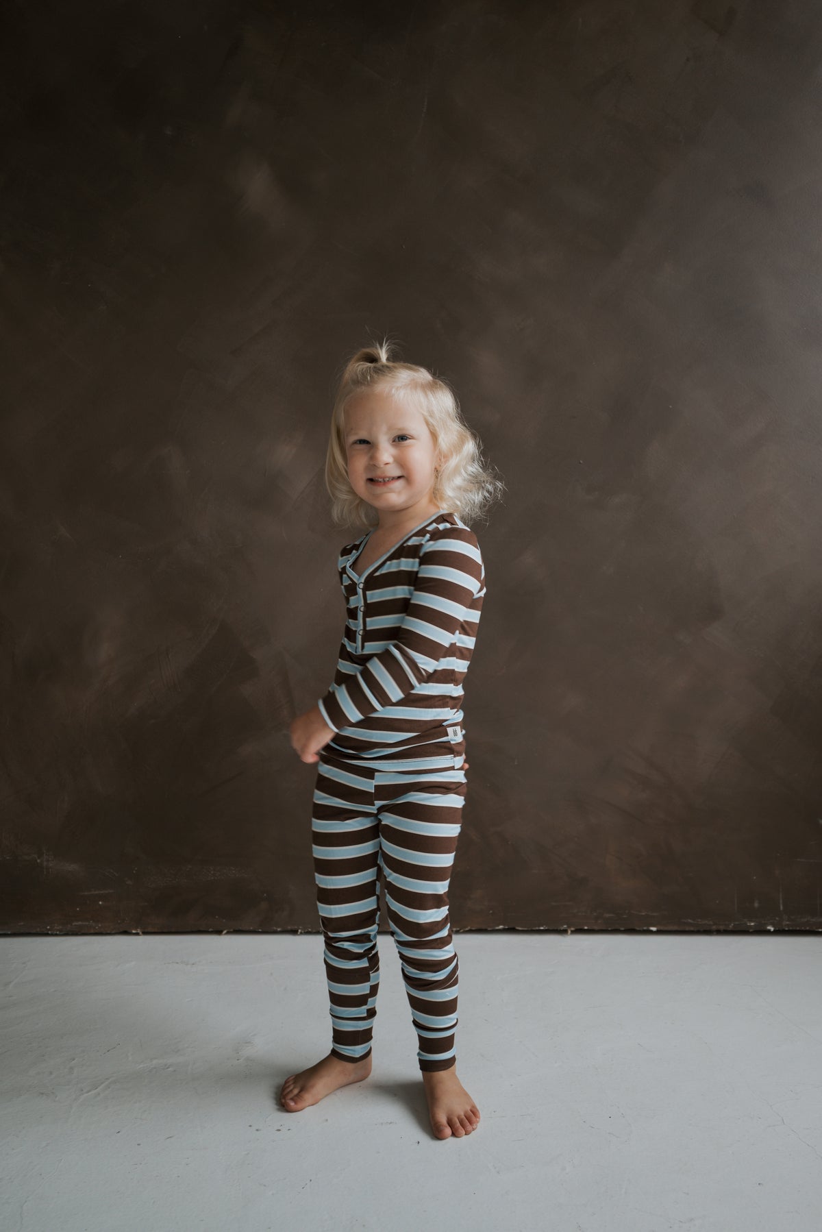 A child wearing Bamboo Two Piece Pajamas | Garrett in breathable, brown and light blue striped bamboo with a button-front top.