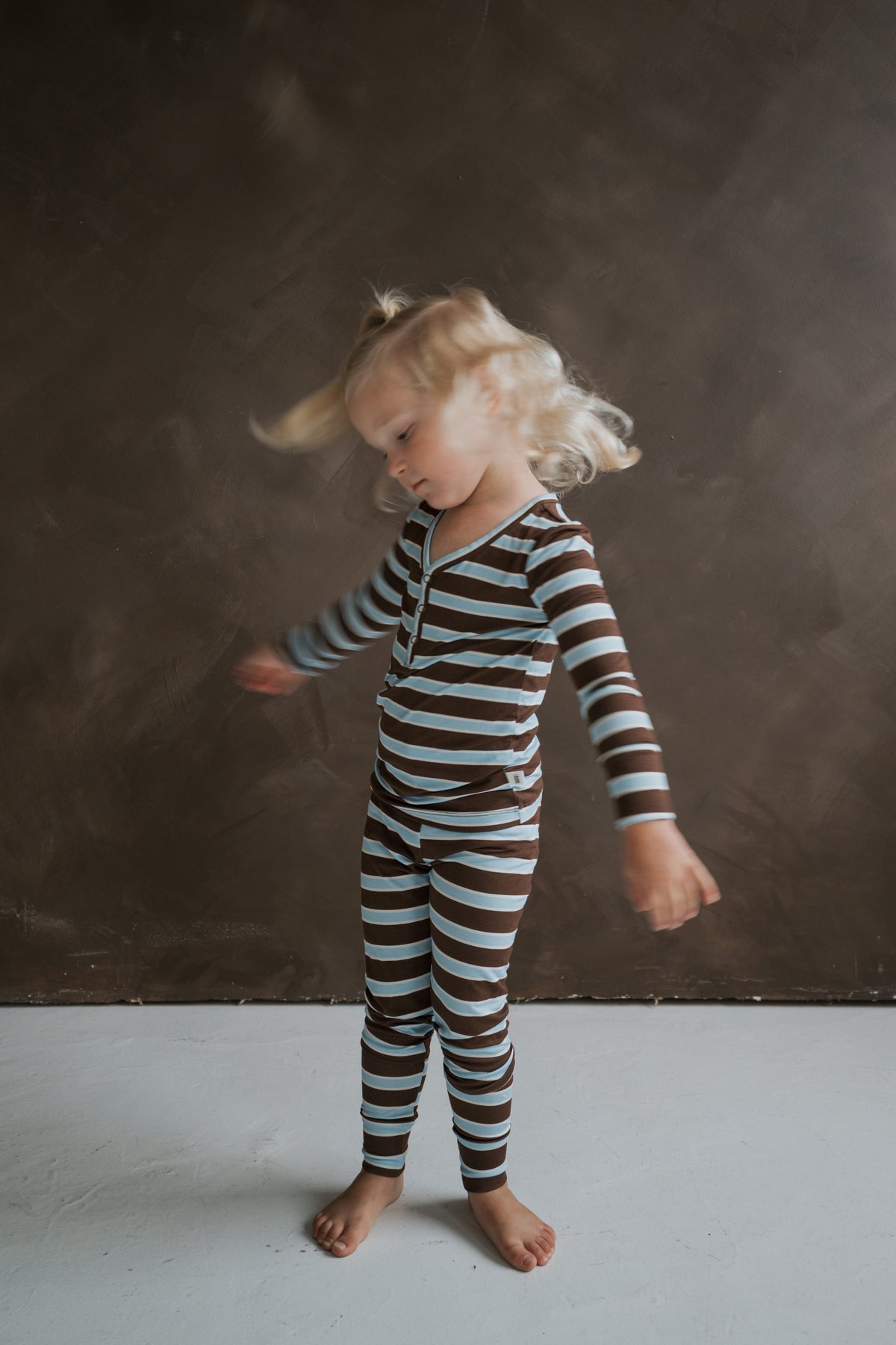 A young child in a long-sleeved brown and blue striped Bamboo Two Piece Pajamas | Garrett spinning in motion.