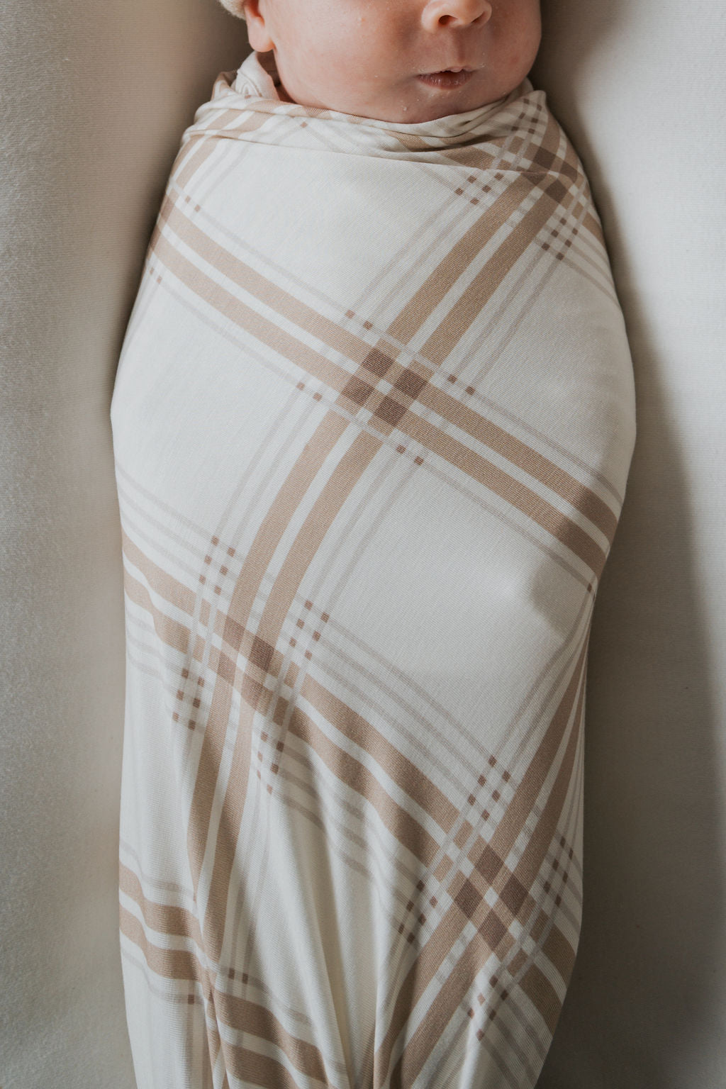 A baby wrapped in a cream and tan Ellis Plaid bamboo swaddle by forever french baby.