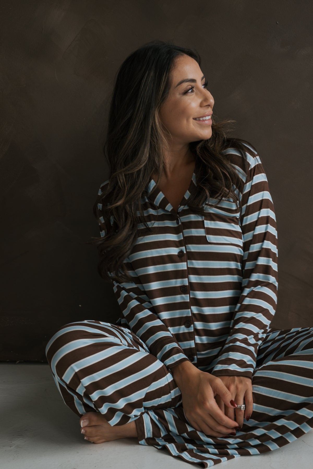 A smiling woman sits on the floor wearing a brown and light blue horizontal striped Women’s Bamboo Button Up Lounge Set | Garrett by forever french baby.