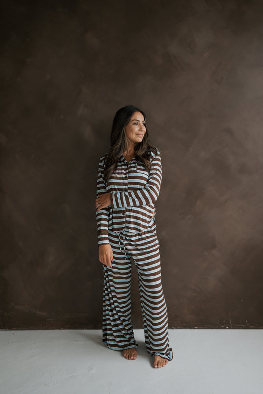 A person wearing the forever french baby Women’s Bamboo Button Up Lounge Set | Garrett, featuring a long-sleeved button-up shirt and matching pants with horizontal brown and light blue stripes.