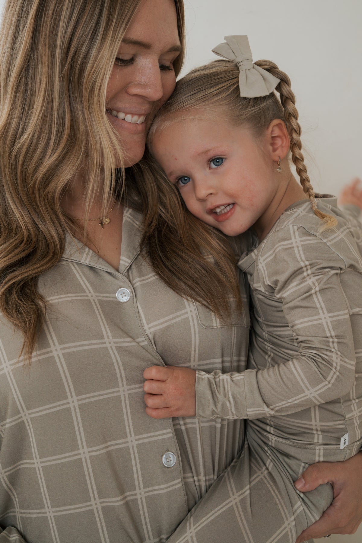 A woman holding a young girl, both wearing matching Bamboo Two Piece Pajamas | Linen Grid in tan with a white grid pattern.