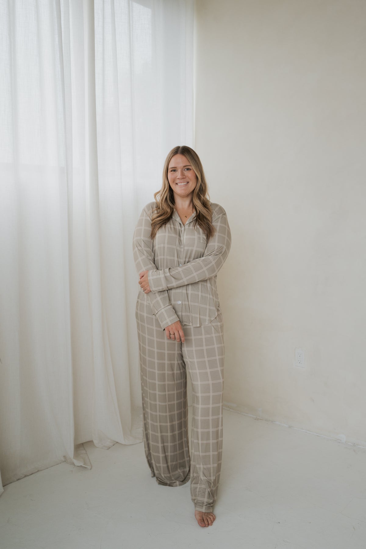 A woman wearing a Women’s Bamboo Button Up Lounge Set | Linen Grid, featuring a tan, long-sleeved button-up shirt and wide-leg lounge pants with a white grid pattern.