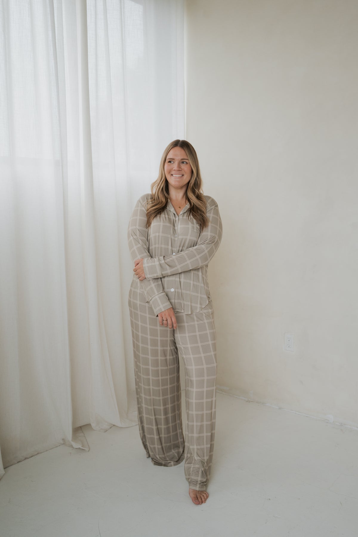 A woman wearing a forever french baby Women’s Bamboo Button Up Lounge Set | Linen Grid, featuring a beige grid-patterned button-up shirt and matching wide-leg lounge pants.