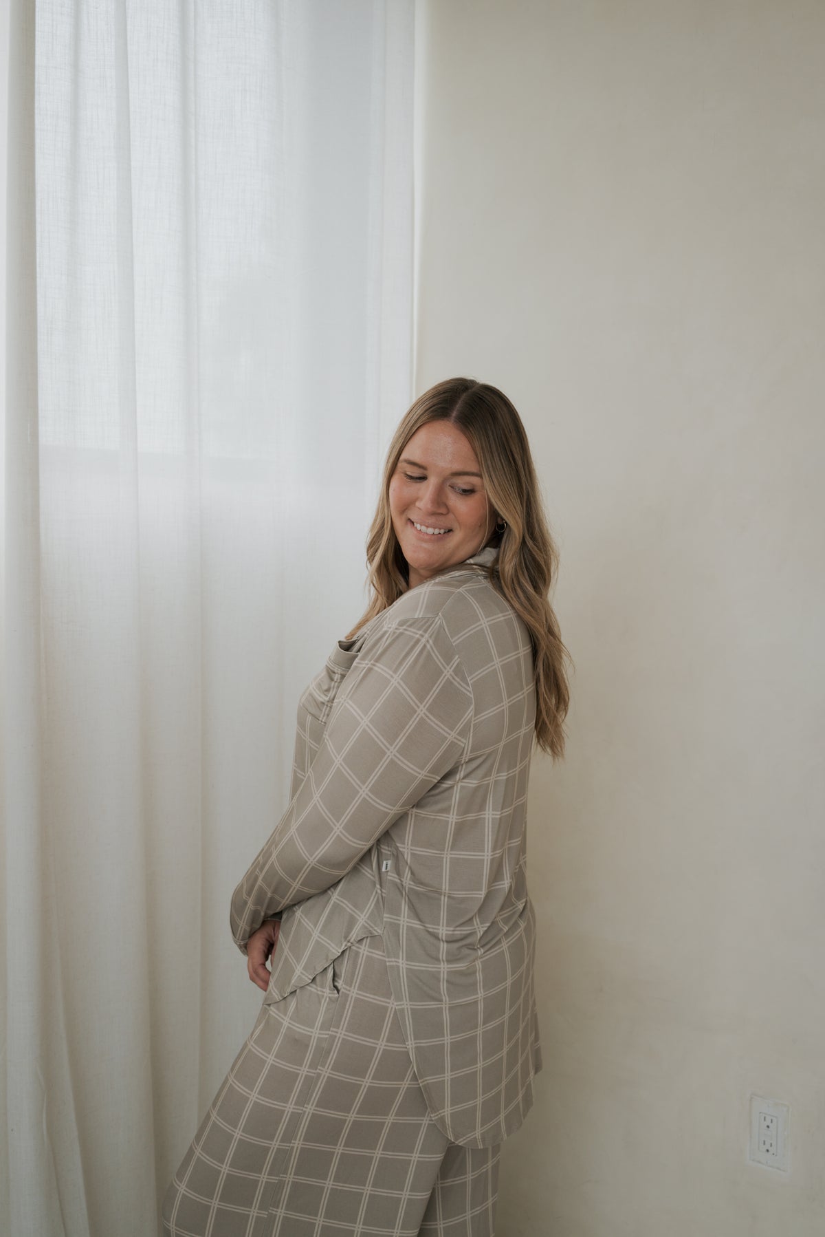 A woman smiling while wearing a Women’s Bamboo Button Up Lounge Set | Linen Grid, featuring a beige long-sleeve button-up shirt and matching wide-leg lounge pants with a white grid pattern.