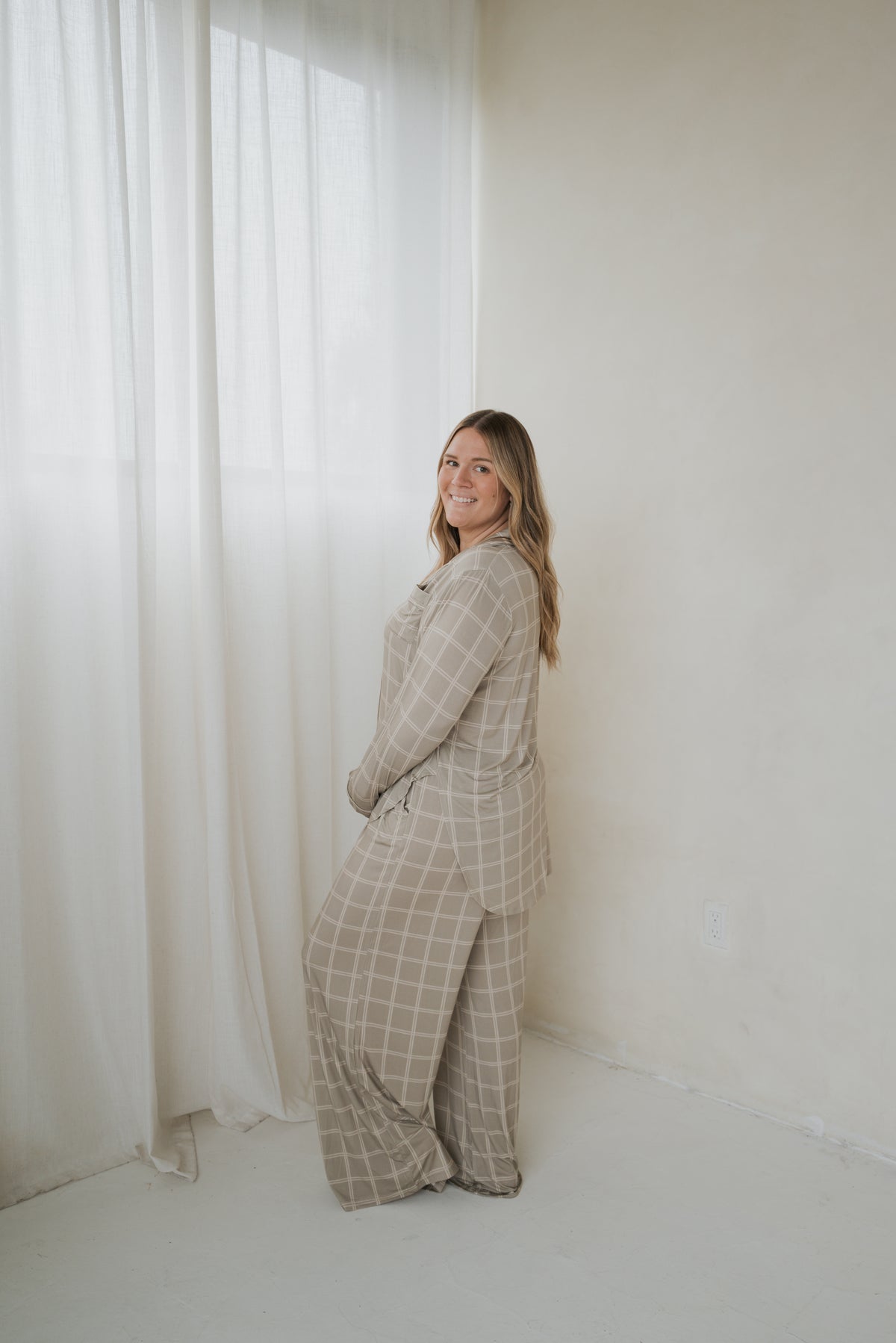 A woman wearing a Women’s Bamboo Button Up Lounge Set | Linen Grid, featuring a tan, long-sleeved button-up shirt and wide-leg lounge pants with a white grid pattern.