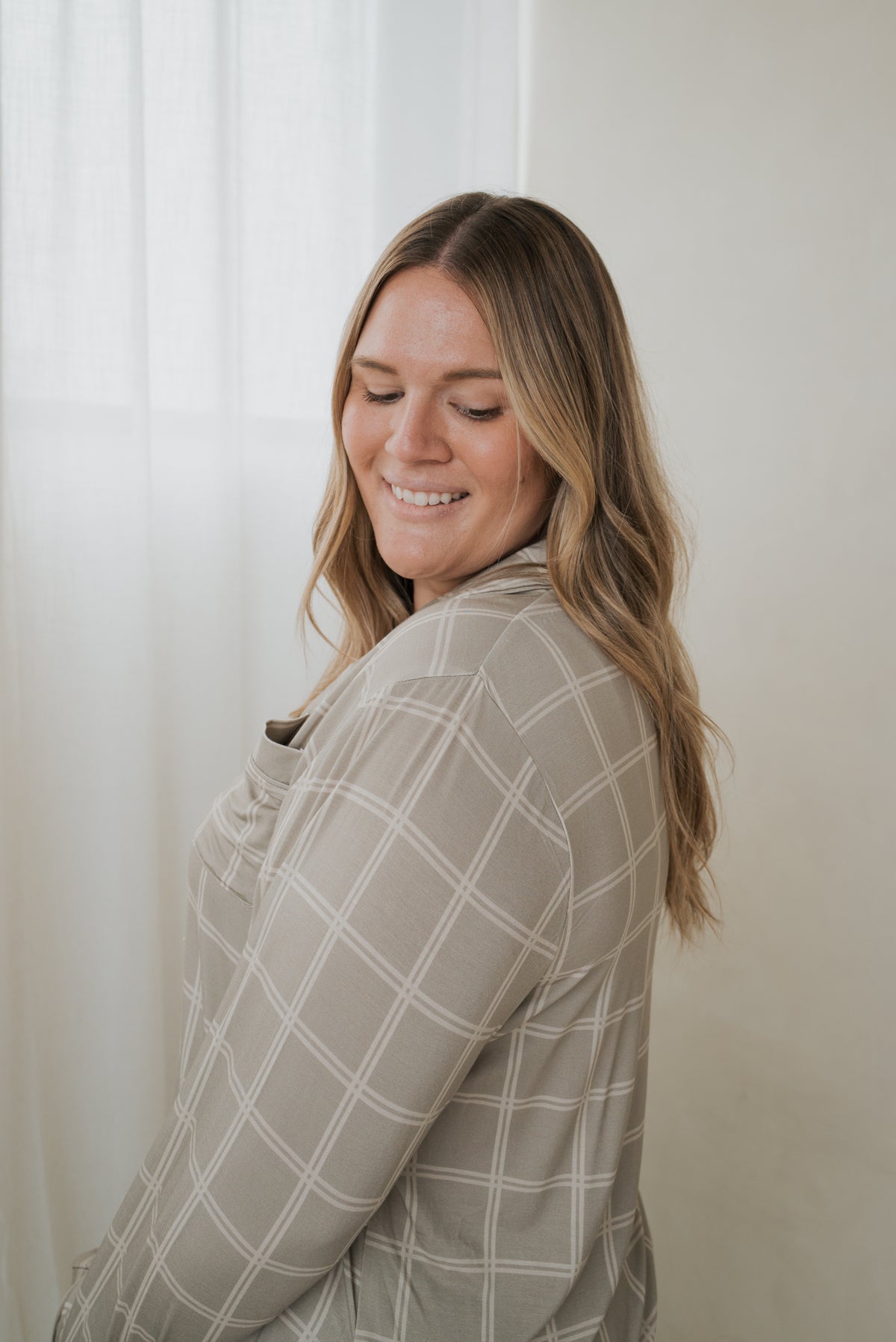 A woman smiles while wearing the beige and white grid button-up shirt from the Women’s Bamboo Button Up Lounge Set | Linen Grid by forever french baby.