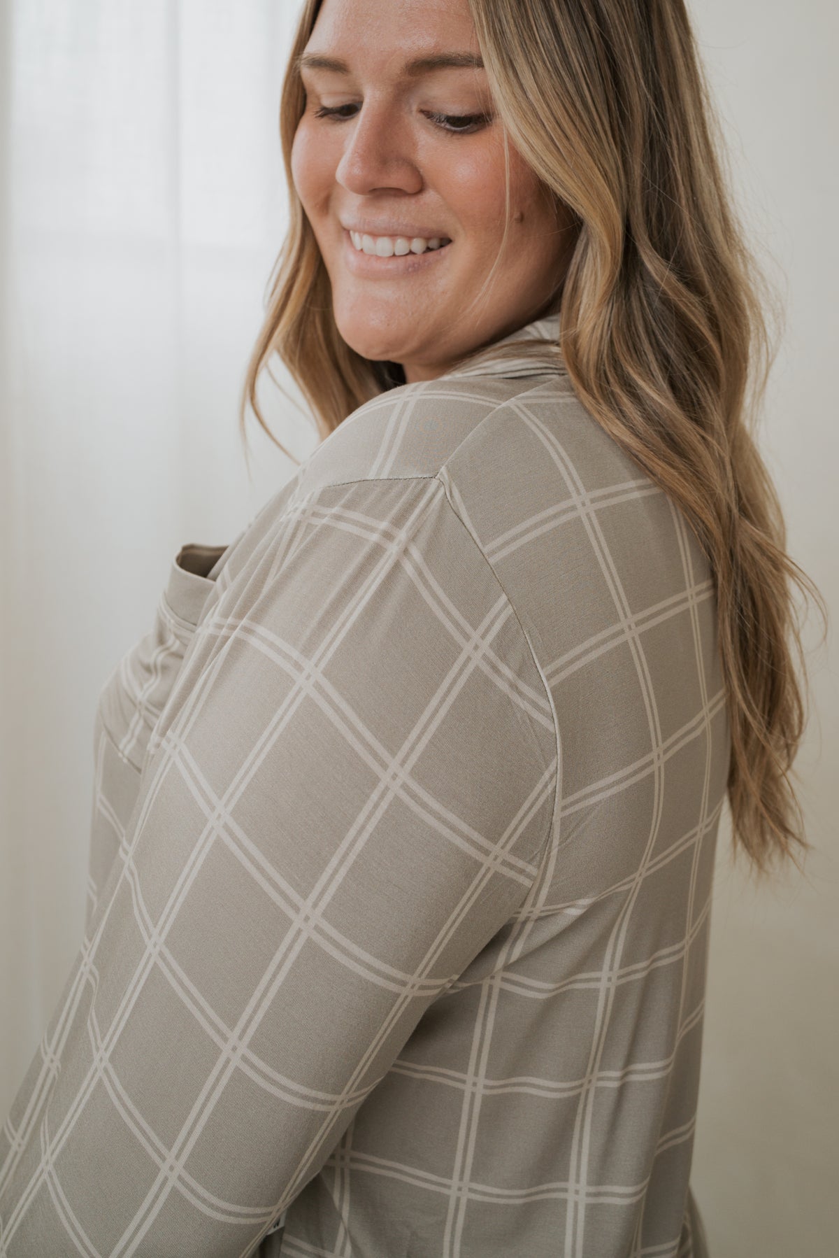 A woman smiles over her shoulder wearing the tan, white-grid Women’s Bamboo Button Up Lounge Set | Linen Grid from our bamboo clothing collection.